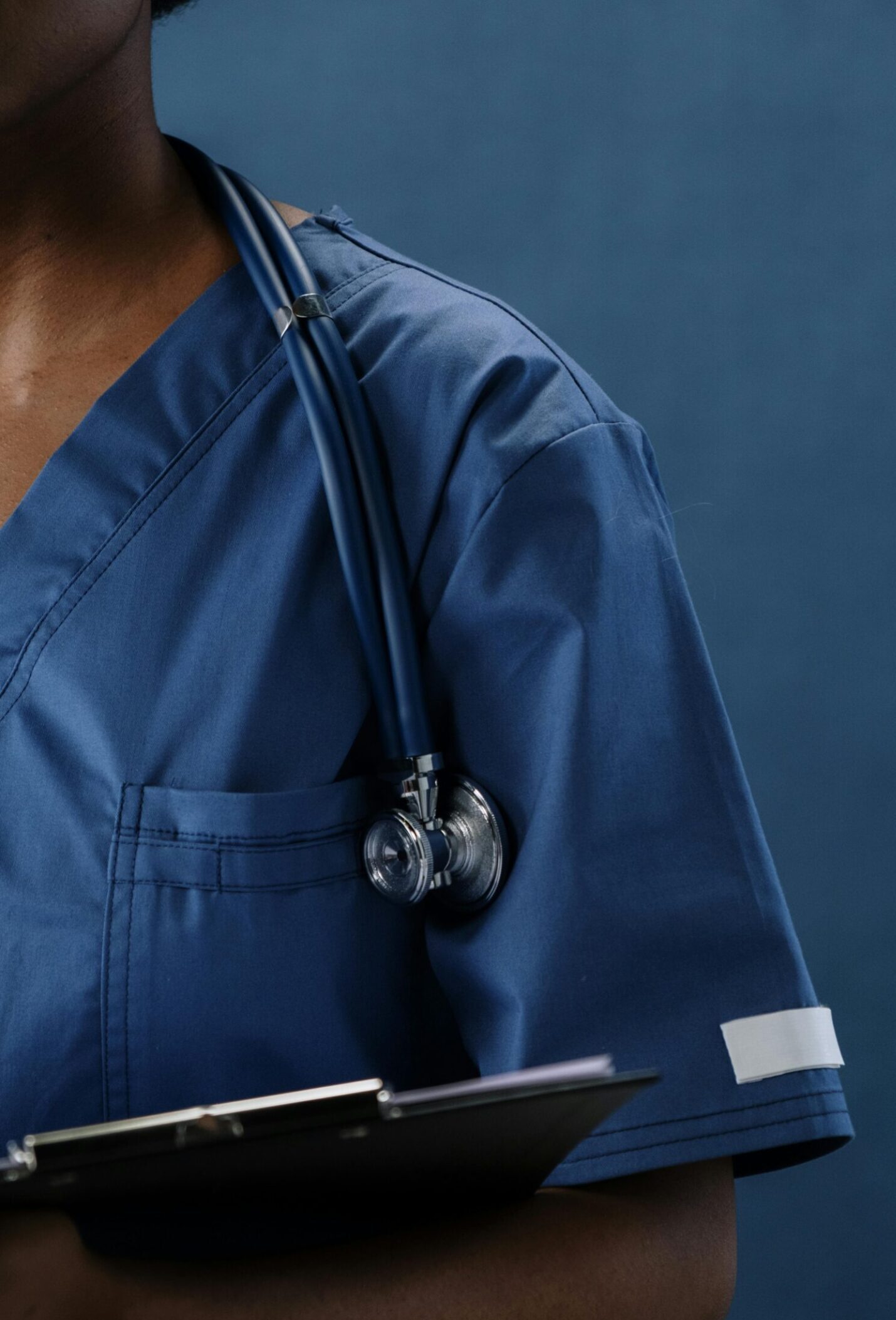 Close-up of a healthcare professional in blue scrubs with a stethoscope and clipboard.